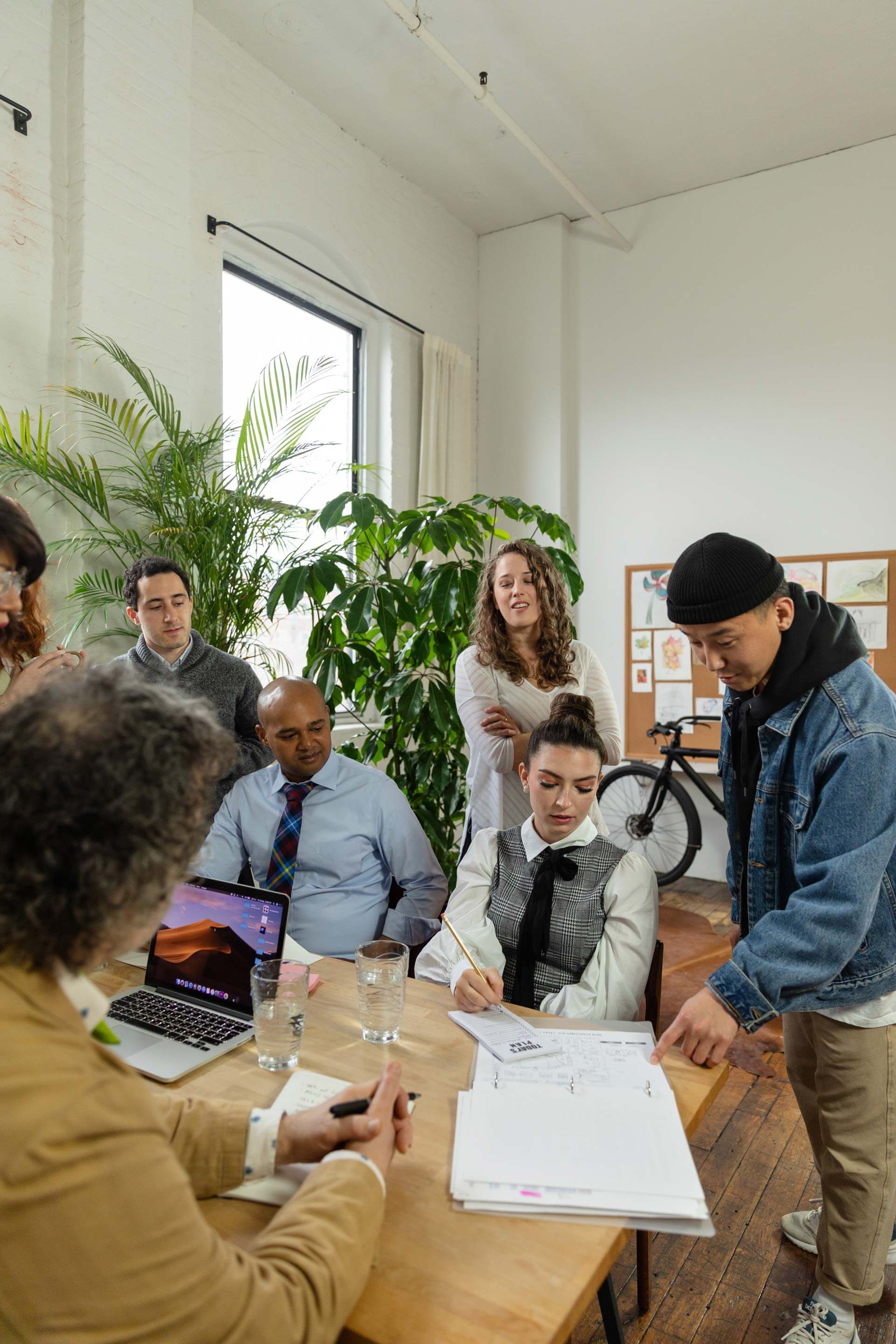 Mensen vergaderen aan tafel met laptops, drinken en notitieboeken.
